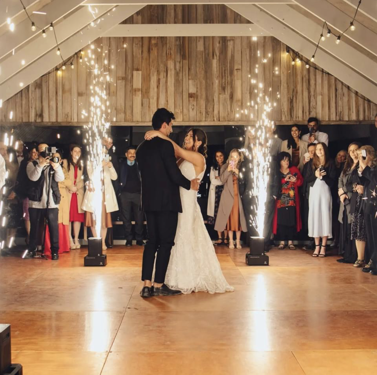 Couple dancing between cold spark fountains in a timber-ceiling reception venue
