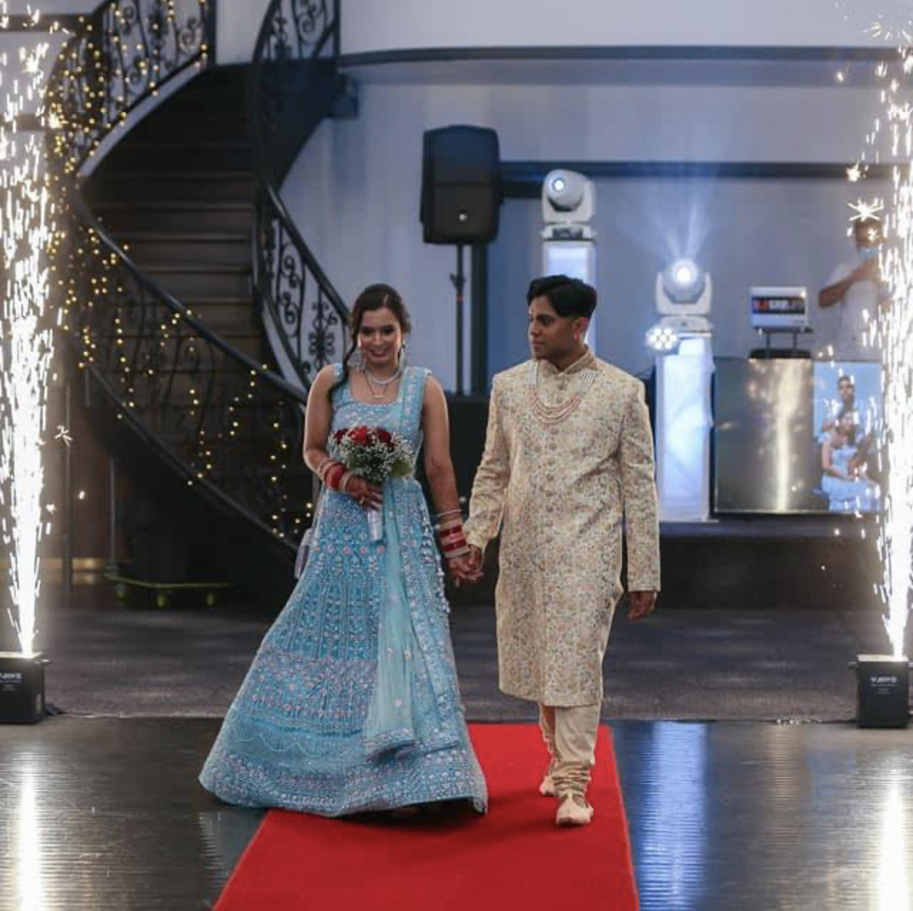 Couple walking down a red carpet between cold spark fountains