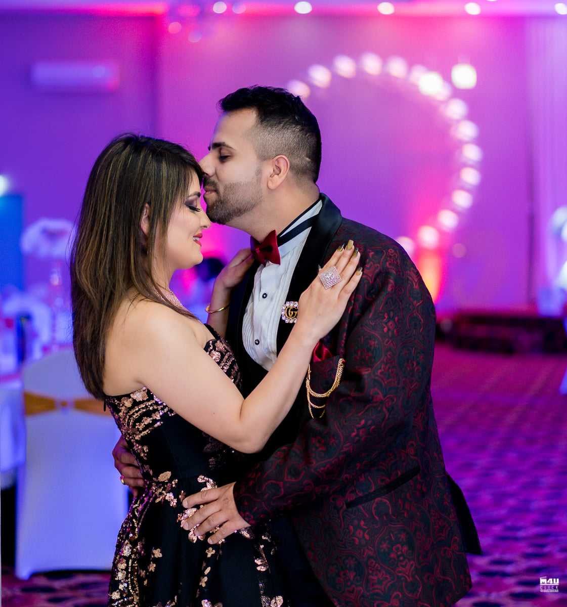 Couple embracing under pink and purple reception lighting
