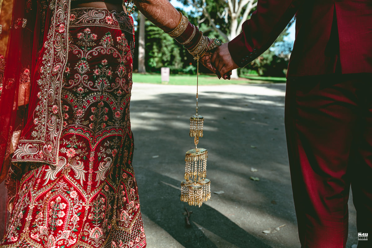 Wedding couple holding hands beside the bride's red embroidered dress and hanging gold jewellery